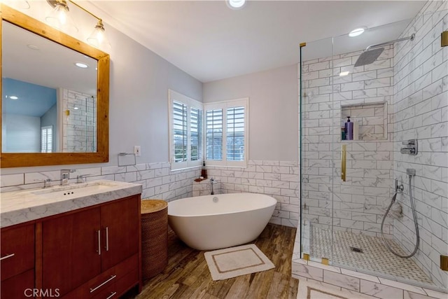 full bathroom with tile walls, a stall shower, a freestanding bath, vanity, and wood finished floors