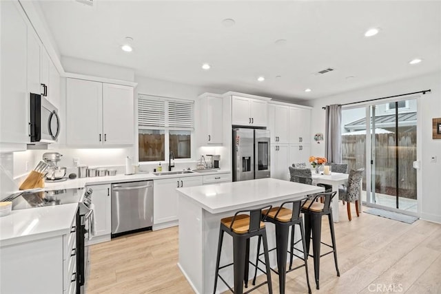 kitchen with stainless steel appliances, a sink, a kitchen bar, light wood-type flooring, and white cabinetry