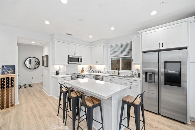 kitchen with appliances with stainless steel finishes, a kitchen breakfast bar, a sink, white cabinets, and recessed lighting