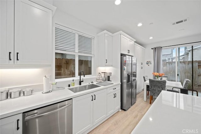 kitchen featuring stainless steel appliances, a sink, light wood-style floors, light countertops, and white cabinetry