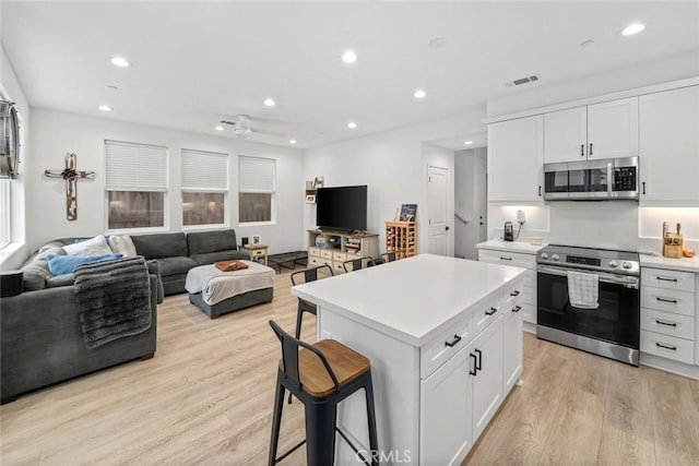 kitchen featuring stainless steel appliances, open floor plan, light wood-type flooring, light countertops, and recessed lighting