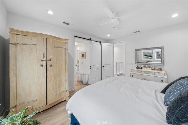 bedroom featuring light wood-style floors, a barn door, recessed lighting, a ceiling fan, and ensuite bathroom