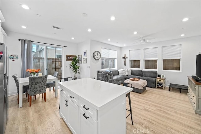 kitchen featuring light wood-type flooring, a ceiling fan, a kitchen island, white cabinetry, and recessed lighting