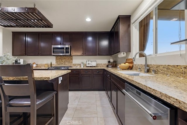 kitchen with appliances with stainless steel finishes, a sink, light tile patterned floors, light stone countertops, and a breakfast bar