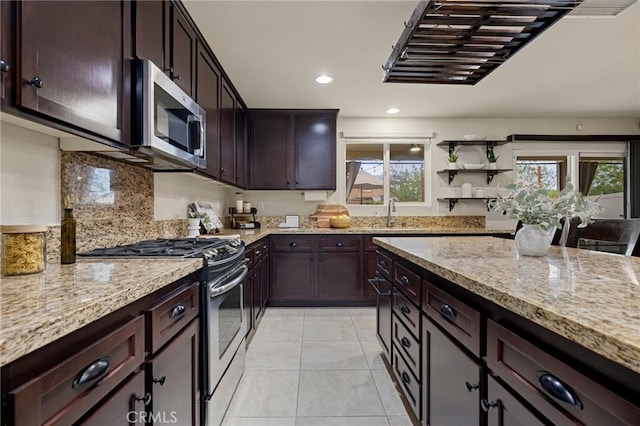 kitchen with appliances with stainless steel finishes, light stone countertops, a sink, backsplash, and dark brown cabinets