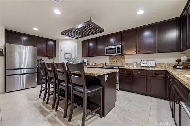 kitchen featuring stainless steel appliances, light tile patterned flooring, dark brown cabinets, light stone counters, and recessed lighting