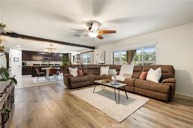 living area with light wood-style floors, ceiling fan, and beamed ceiling