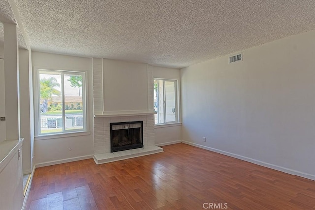 12406 Benson Ave, Chino, CA 91710 - unfurnished living room featuring wood finished floors, a textured ceiling, a brick fireplace, plenty of natural light, and baseboards