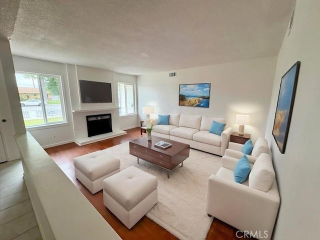 12406 Benson Ave, Chino, CA 91710 - living room featuring plenty of natural light, a textured ceiling, a fireplace with raised hearth, wood finished floors, and baseboards