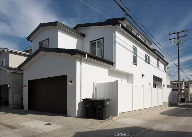 view of property exterior with stucco siding, fence, a garage, and concrete driveway