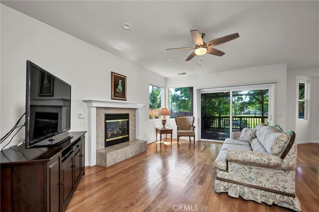 living room featuring a tile fireplace, ceiling fan, and light wood finished floors
