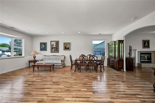 dining area featuring light wood finished floors, arched walkways, recessed lighting, baseboards, and a glass covered fireplace