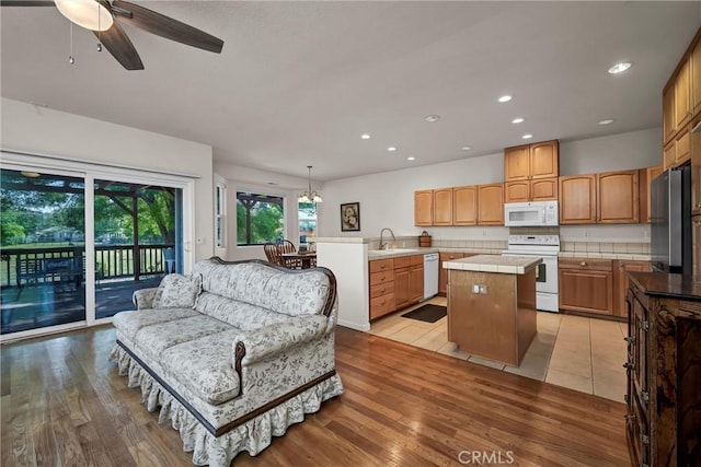 kitchen featuring white appliances, a sink, a kitchen island, recessed lighting, and light wood-type flooring