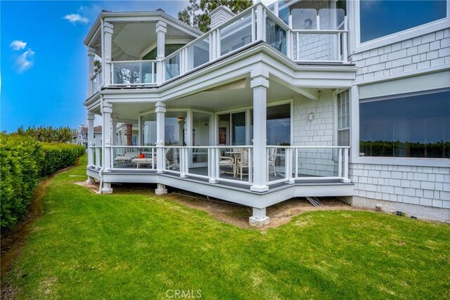 rear view of house with a balcony, covered porch, and a lawn