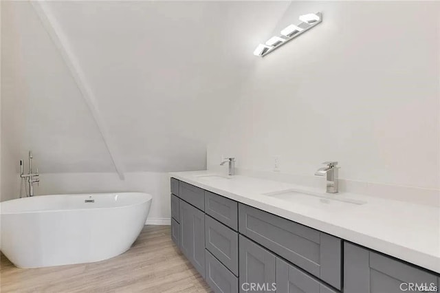 full bath featuring double vanity, a freestanding bath, wood finished floors, and lofted ceiling