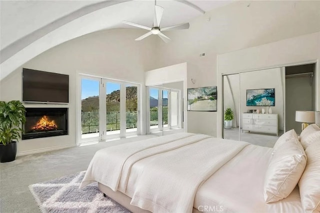 carpeted bedroom with high vaulted ceiling, a glass covered fireplace, and ceiling fan