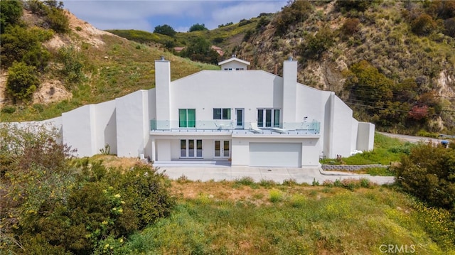 back of house with a chimney, a garage, stucco siding, a mountain view, and a balcony