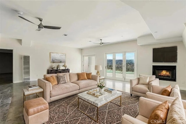 living room featuring ceiling fan, a heating unit, baseboards, and a lit fireplace