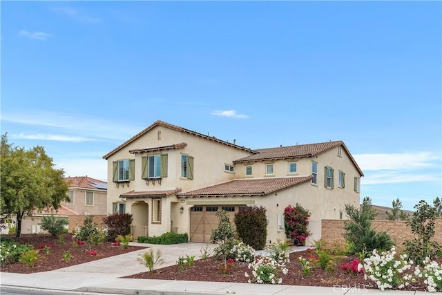 mediterranean / spanish house with an attached garage, concrete driveway, a tile roof, stucco siding, and fence