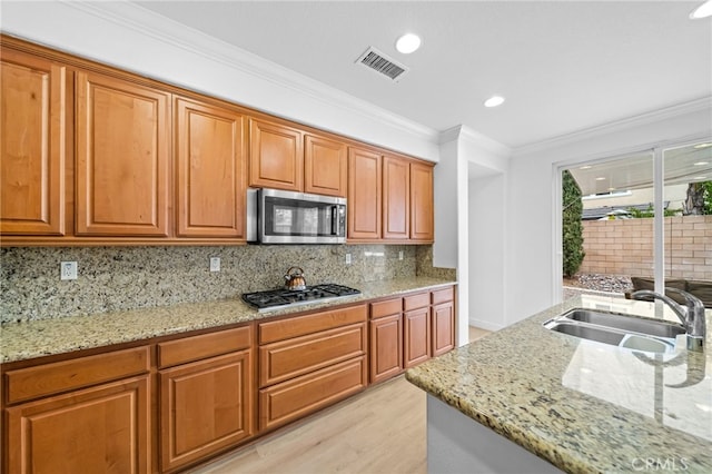 kitchen featuring a sink, stainless steel appliances, crown molding, light stone counters, and tasteful backsplash