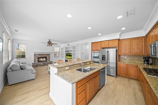kitchen with stainless steel appliances, a sink, ornamental molding, light wood-style flooring, and a kitchen island with sink