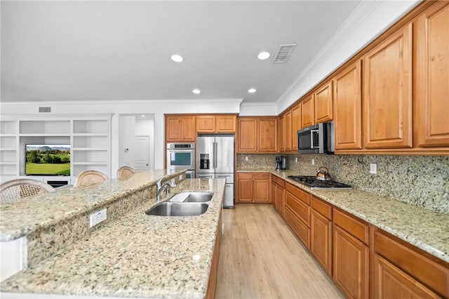 kitchen featuring stainless steel appliances, a sink, crown molding, a kitchen island with sink, and brown cabinetry