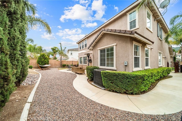 view of home's exterior with stucco siding, a fenced backyard, a patio, central AC, and an outdoor hangout area