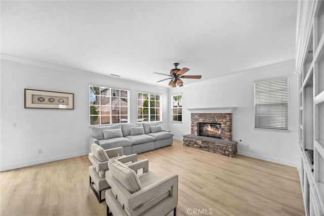 living area featuring crown molding, ceiling fan, a stone fireplace, baseboards, and light wood-style floors
