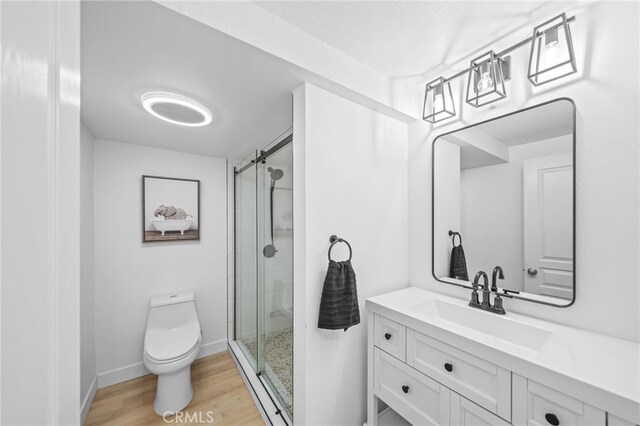 bathroom with toilet, a shower stall, wood finished floors, vanity, and baseboards