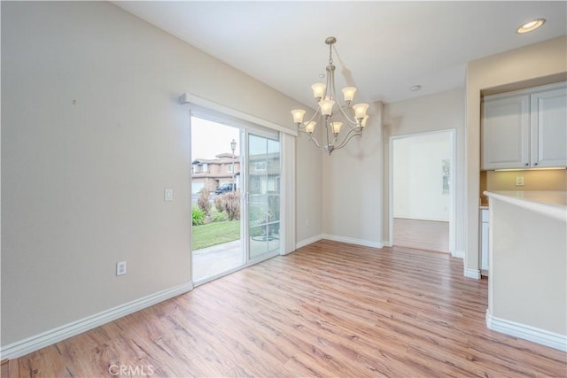 unfurnished dining area featuring a chandelier, light wood-type flooring, and baseboards