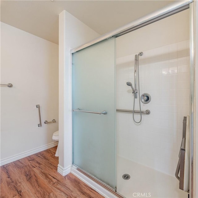 bathroom featuring a shower stall, wood finished floors, toilet, and baseboards