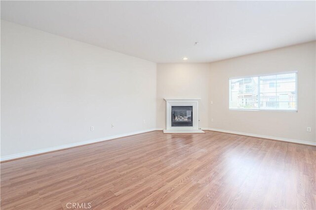 unfurnished living room with a glass covered fireplace, light wood finished floors, baseboards, and recessed lighting