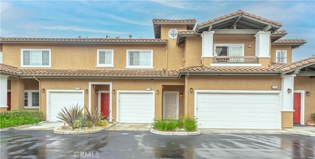 view of property featuring an attached garage, a tile roof, stucco siding, and driveway