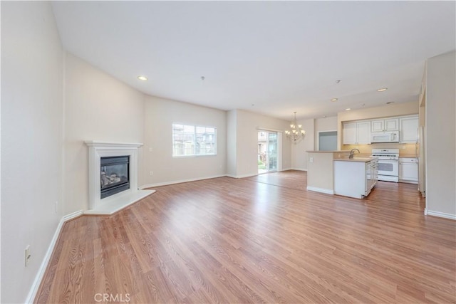 unfurnished living room featuring a chandelier, a glass covered fireplace, light wood-style flooring, baseboards, and a sink