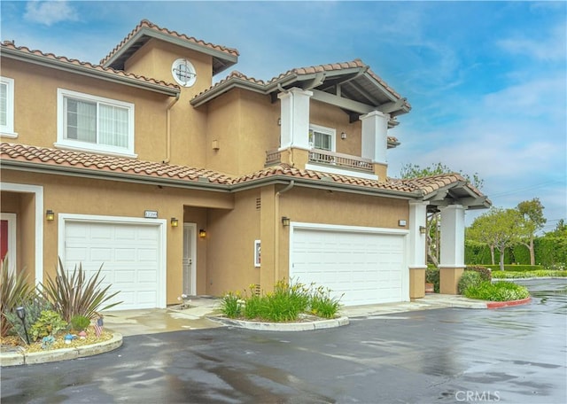 mediterranean / spanish-style house featuring a tiled roof, a garage, stucco siding, and asphalt driveway
