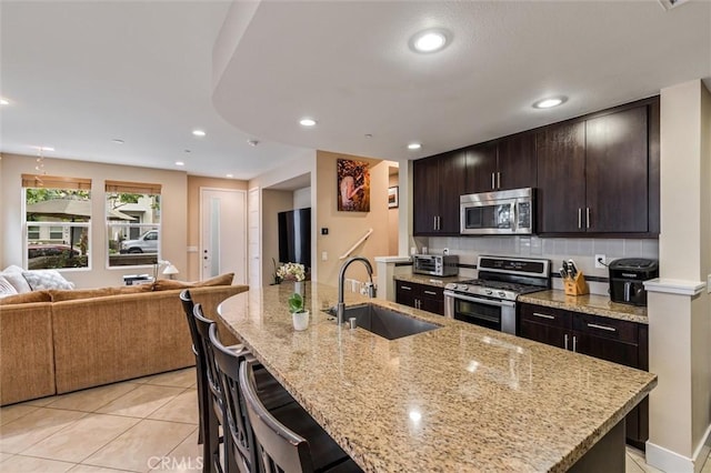 kitchen featuring appliances with stainless steel finishes, a sink, open floor plan, a breakfast bar, and light tile patterned floors