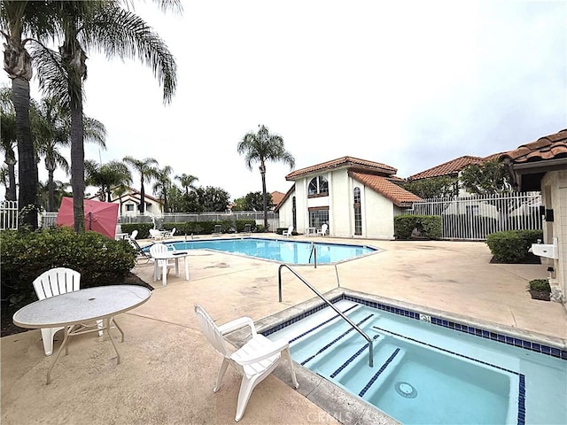 community pool with a hot tub, a patio area, and fence