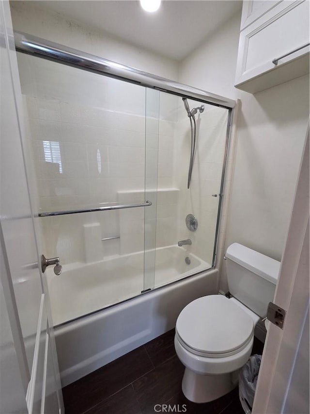 bathroom featuring wood finished floors, toilet, and bath / shower combo with glass door