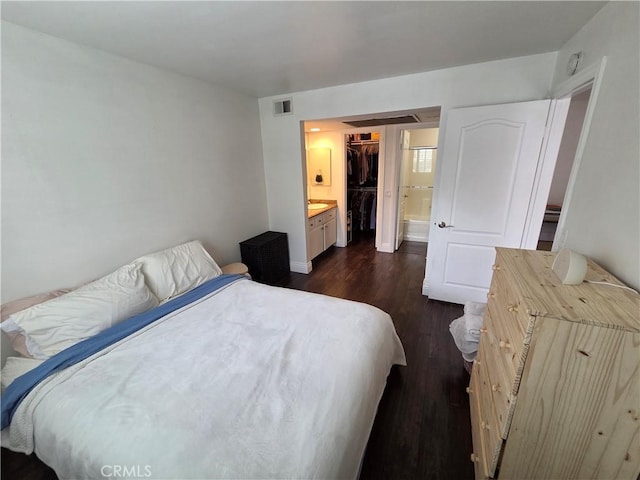 bedroom with dark wood-style floors, a walk in closet, a closet, connected bathroom, and baseboards