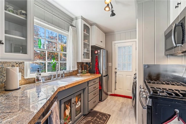 kitchen with appliances with stainless steel finishes, a sink, crown molding, white cabinets, and glass insert cabinets