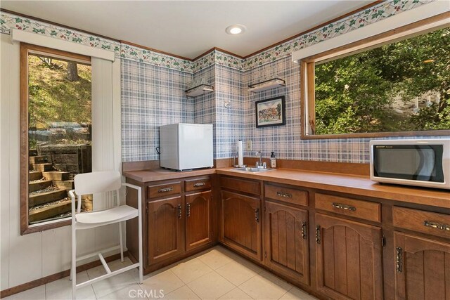 kitchen featuring a sink, wallpapered walls, plenty of natural light, light tile patterned floors, and light countertops