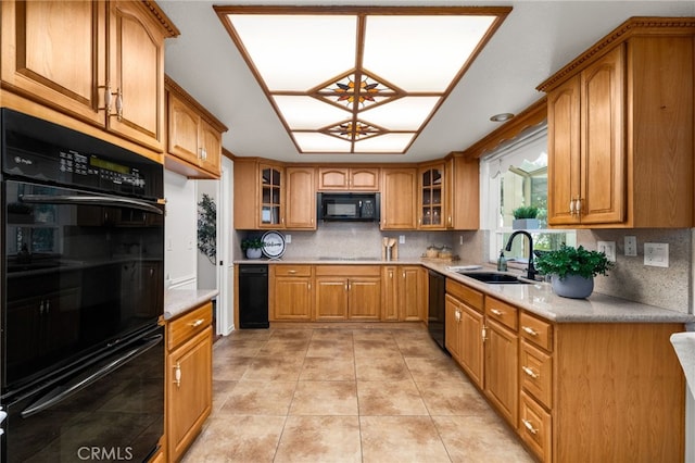 kitchen featuring a sink, black appliances, brown cabinetry, decorative backsplash, and glass insert cabinets