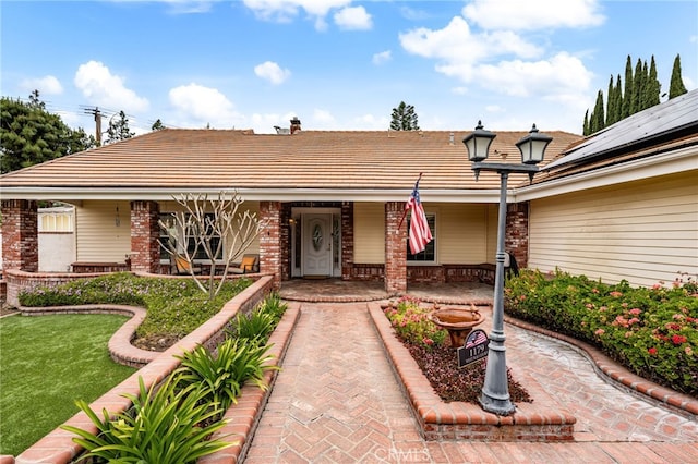 single story home with a porch, brick siding, a front yard, and a tiled roof