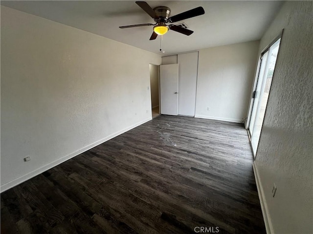 unfurnished bedroom featuring dark wood-style flooring, baseboards, ceiling fan, and a closet