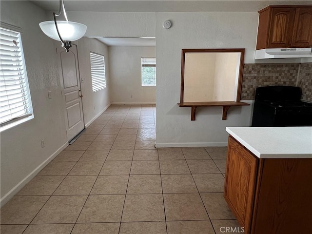 kitchen with under cabinet range hood, black electric range oven, light tile patterned flooring, light countertops, and baseboards