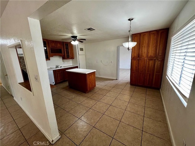 kitchen featuring a kitchen island, light tile patterned floors, light countertops, ceiling fan, and glass insert cabinets