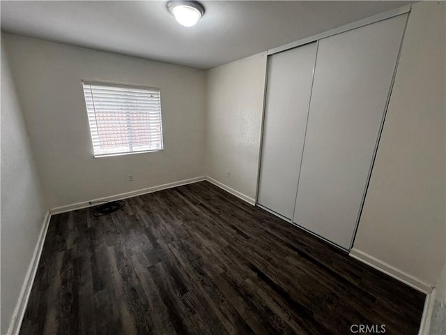 unfurnished bedroom with dark wood finished floors, baseboards, and a closet