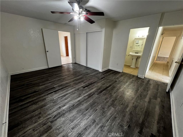 unfurnished bedroom with wood finished floors, a closet, connected bathroom, baseboards, and ceiling fan