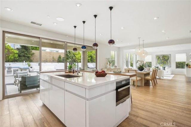 kitchen featuring a sink, an island with sink, white cabinetry, stainless steel oven, and plenty of natural light
