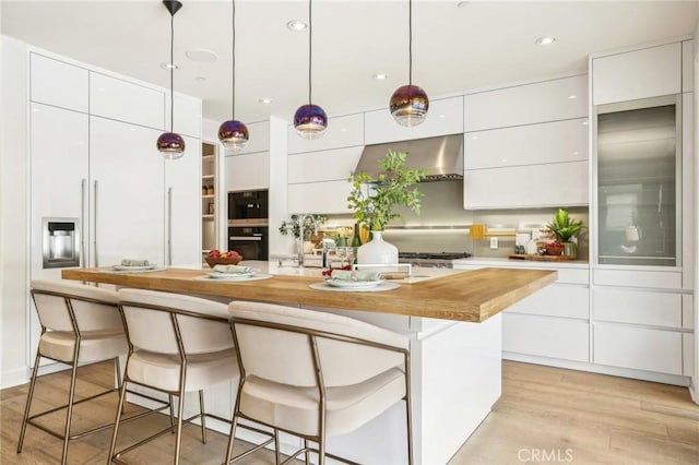 kitchen featuring modern cabinets, wall chimney exhaust hood, white cabinets, a breakfast bar, and an island with sink